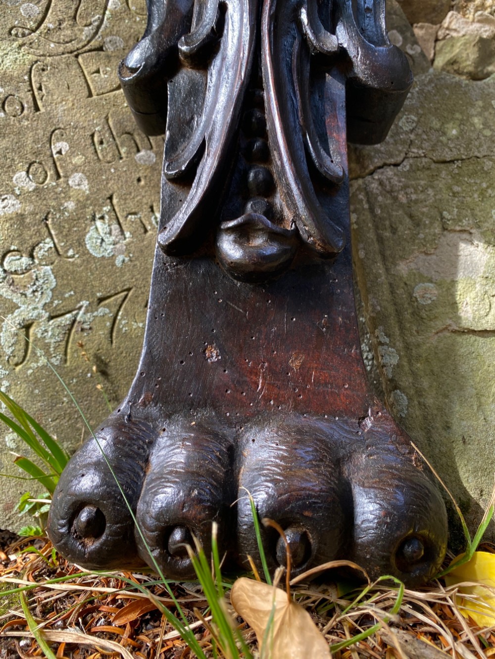 A hand-carved dark oak wood element featuring a stylised Green Man face tapering down into a lion paw base. View II