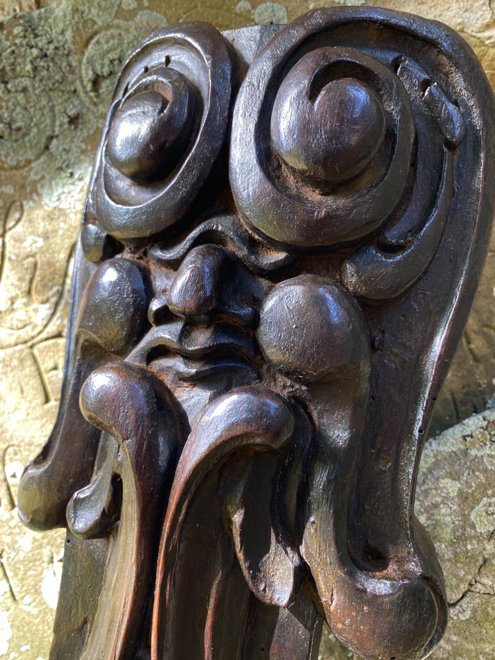 A hand-carved dark oak wood element featuring a stylised Green Man face tapering down into a lion paw base. View III