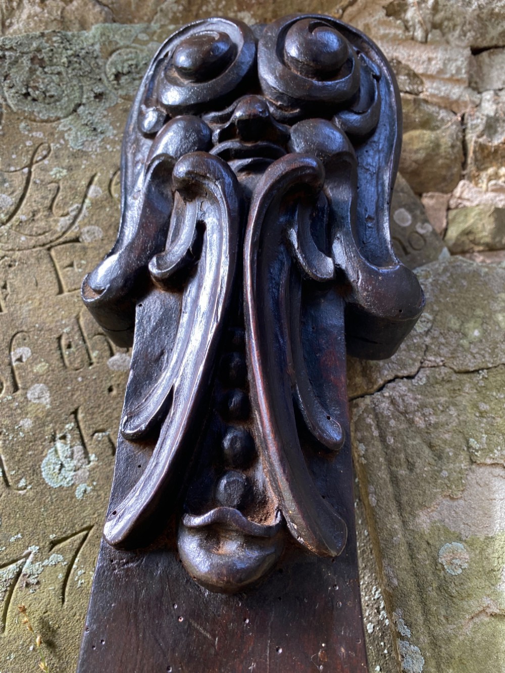 A hand-carved dark oak wood element featuring a stylised Green Man face tapering down into a lion paw base. View IV