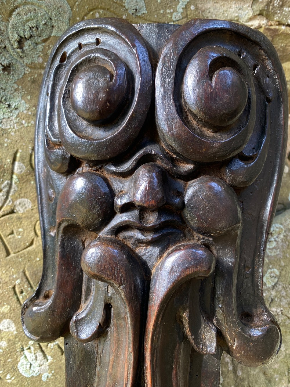 A hand-carved dark oak wood element featuring a stylised Green Man face tapering down into a lion paw base. View V