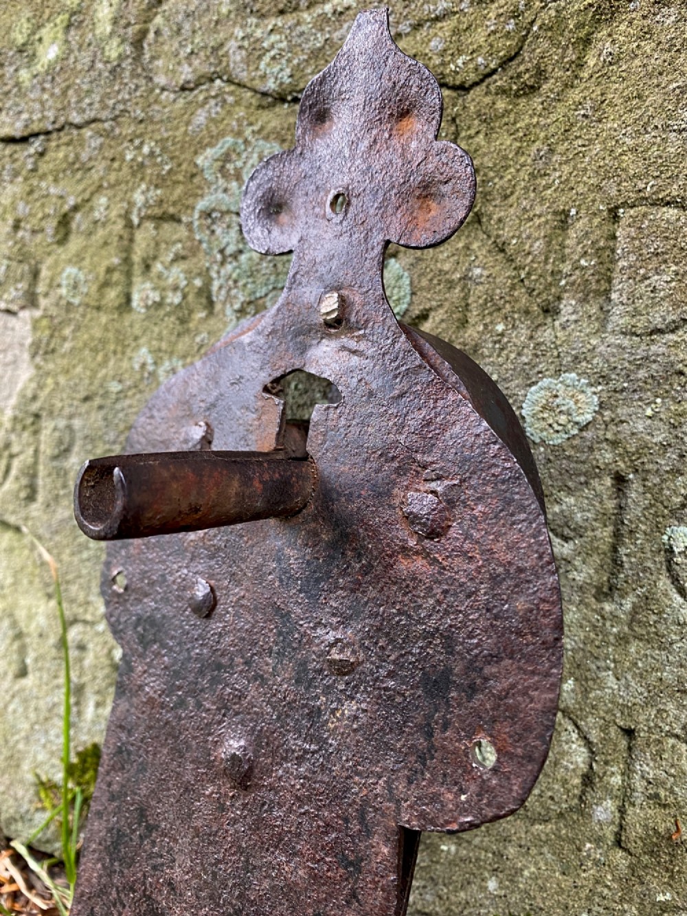 A hand-forged dark wrought iron lock plate featuring a trefoil crest, projecting key pipe, and surface oxidisation. View V