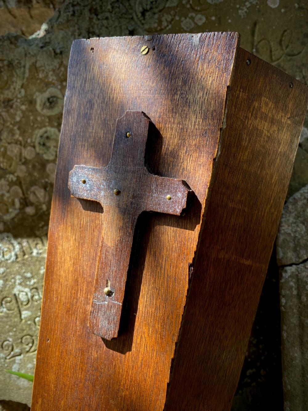 A wooden coffin-shaped collection box featuring a raised wooden cross motif and a narrow coin slot on the front lid. View II