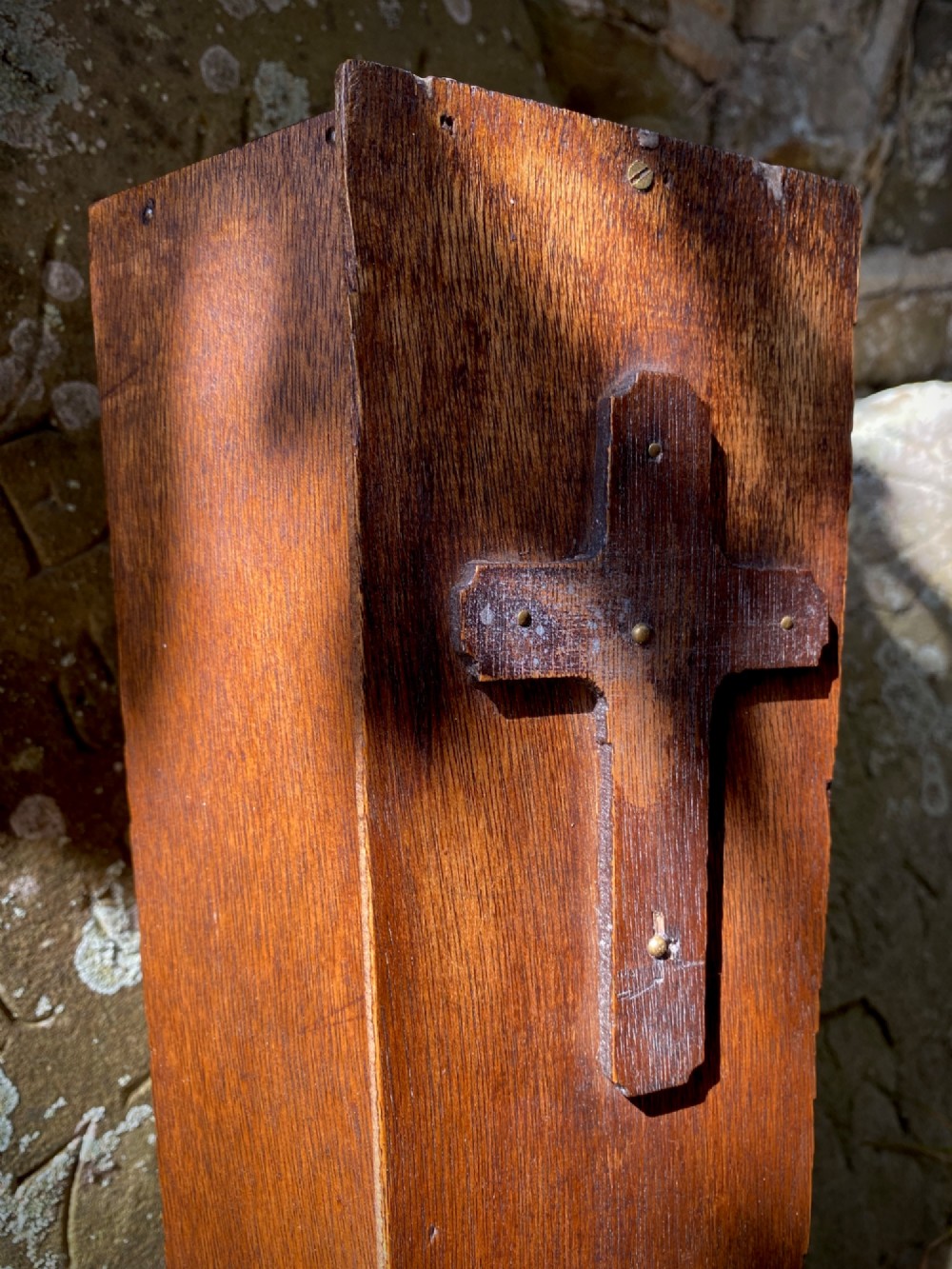 A wooden coffin-shaped collection box featuring a raised wooden cross motif and a narrow coin slot on the front lid. View IV