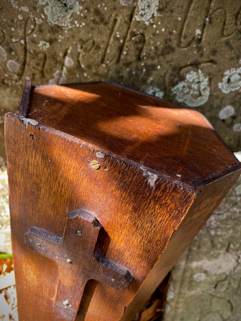 A wooden coffin-shaped collection box featuring a raised wooden cross motif and a narrow coin slot on the front lid. View V