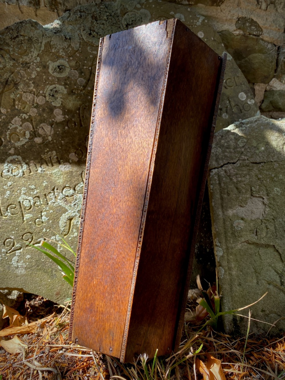 A wooden coffin-shaped collection box featuring a raised wooden cross motif and a narrow coin slot on the front lid. View VIII