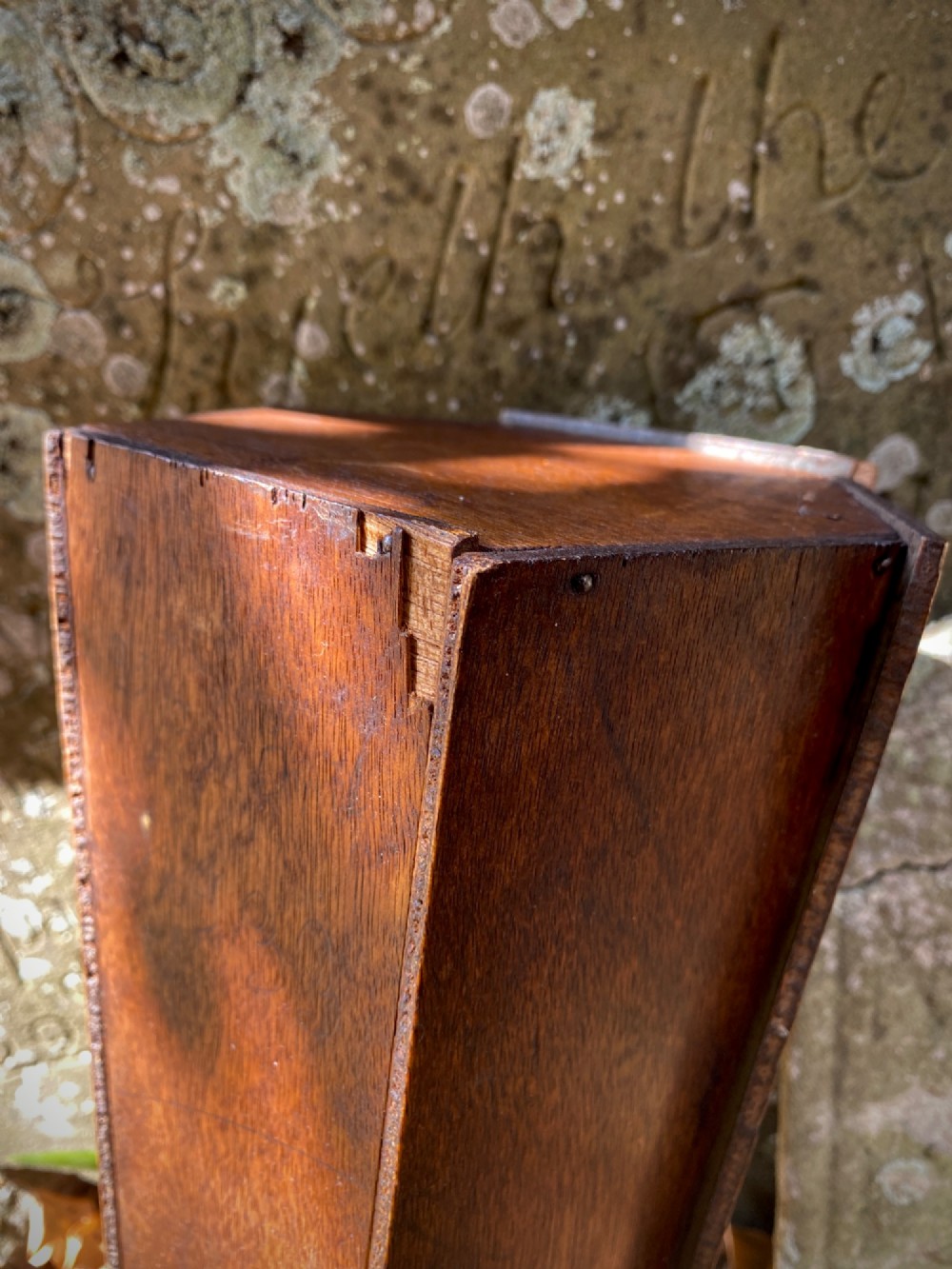 A wooden coffin-shaped collection box featuring a raised wooden cross motif and a narrow coin slot on the front lid. View IX