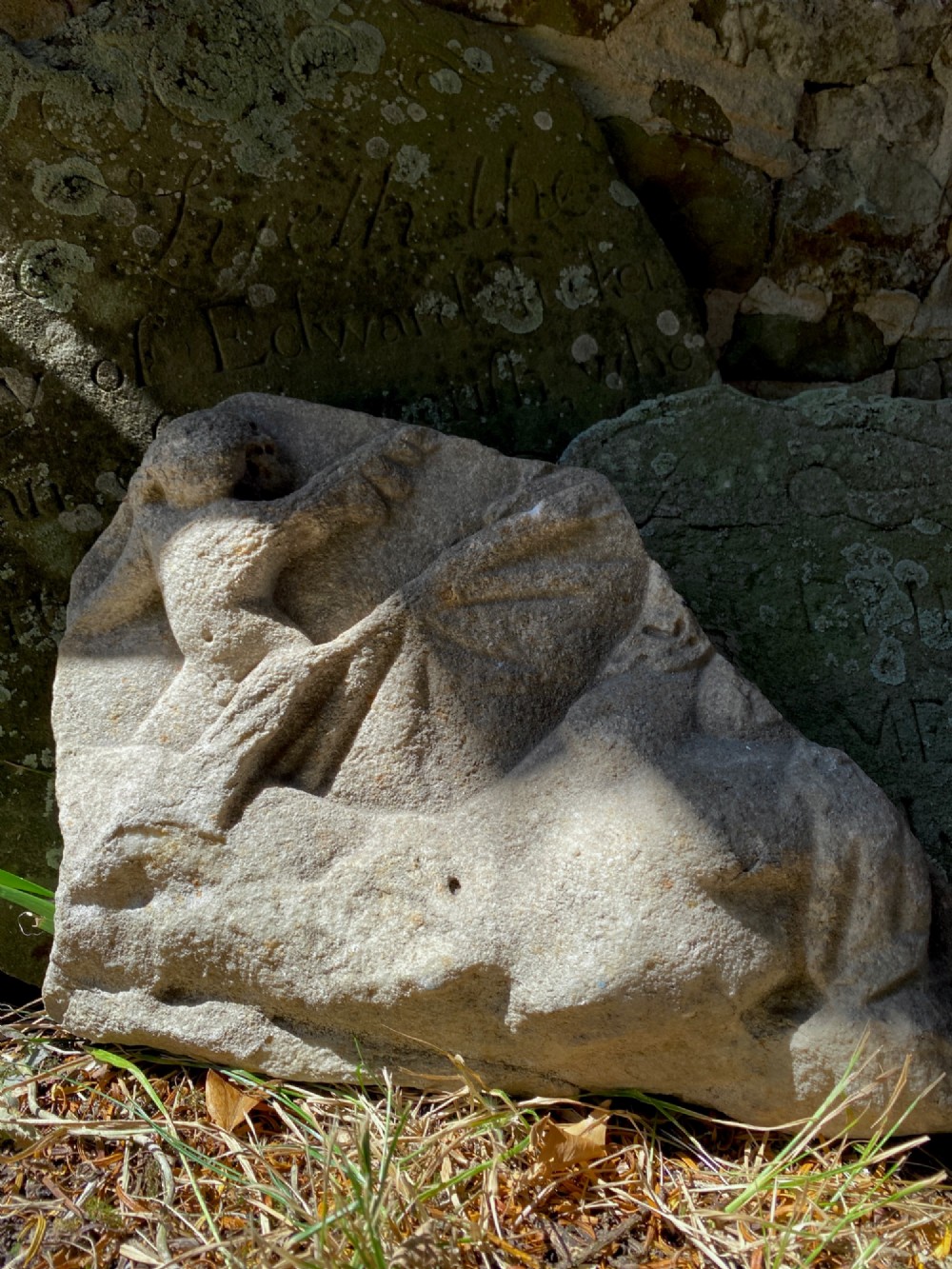 A carved weathered stone fragment depicting a high-relief figure of a winged cherub above a reclining form.
