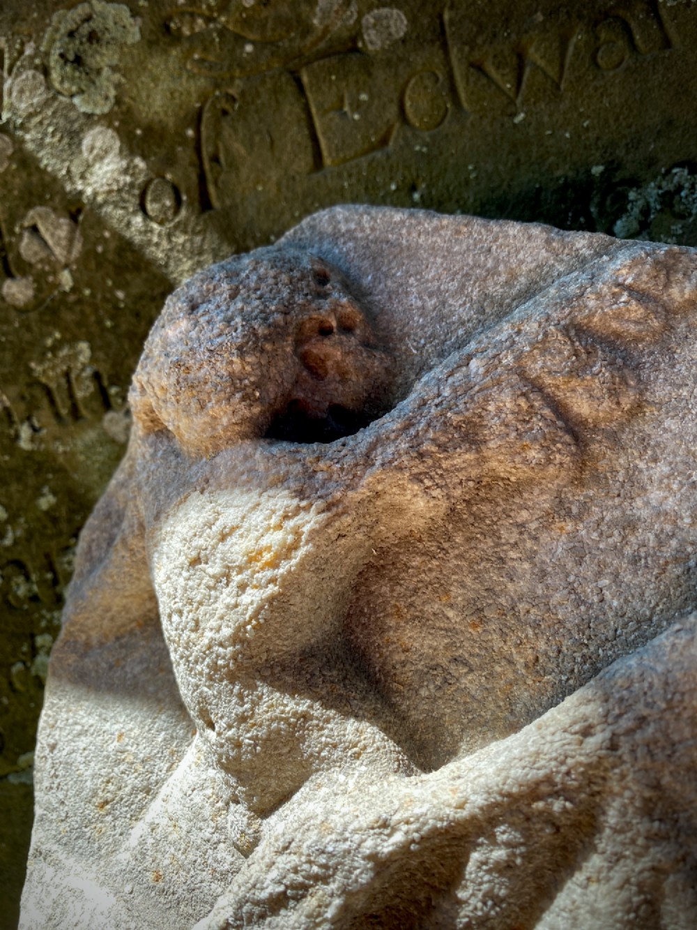 A carved weathered stone fragment depicting a high-relief figure of a winged cherub above a reclining form. View II