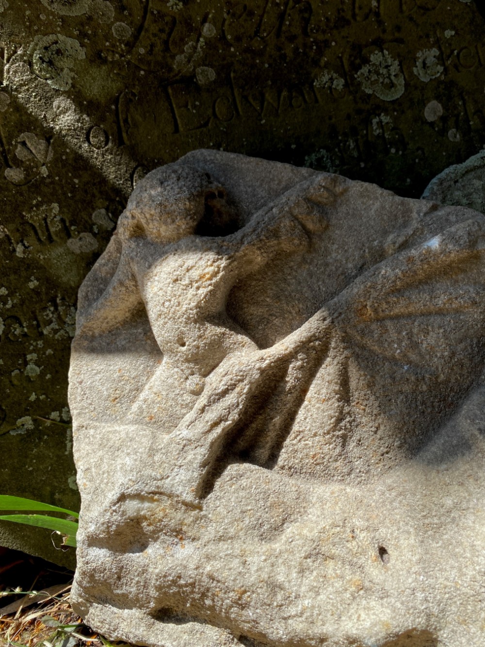 A carved weathered stone fragment depicting a high-relief figure of a winged cherub above a reclining form. View III
