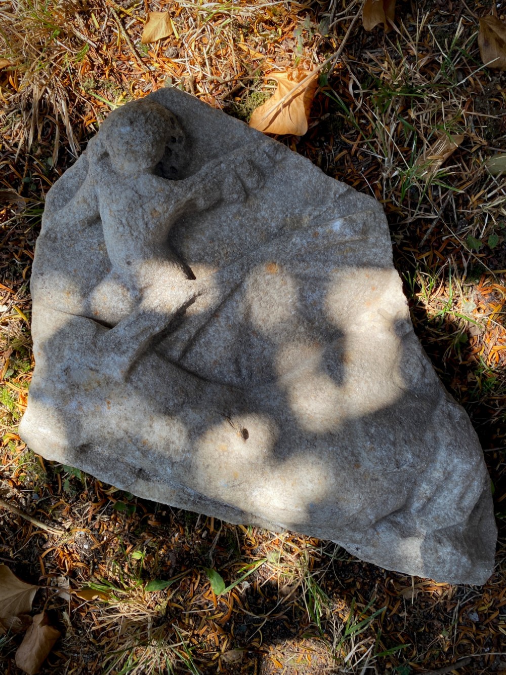 A carved weathered stone fragment depicting a high-relief figure of a winged cherub above a reclining form. View VI