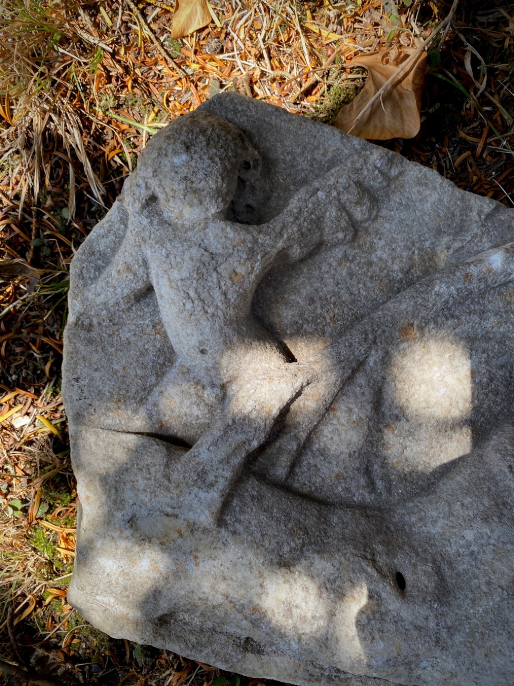 A carved weathered stone fragment depicting a high-relief figure of a winged cherub above a reclining form. View VII