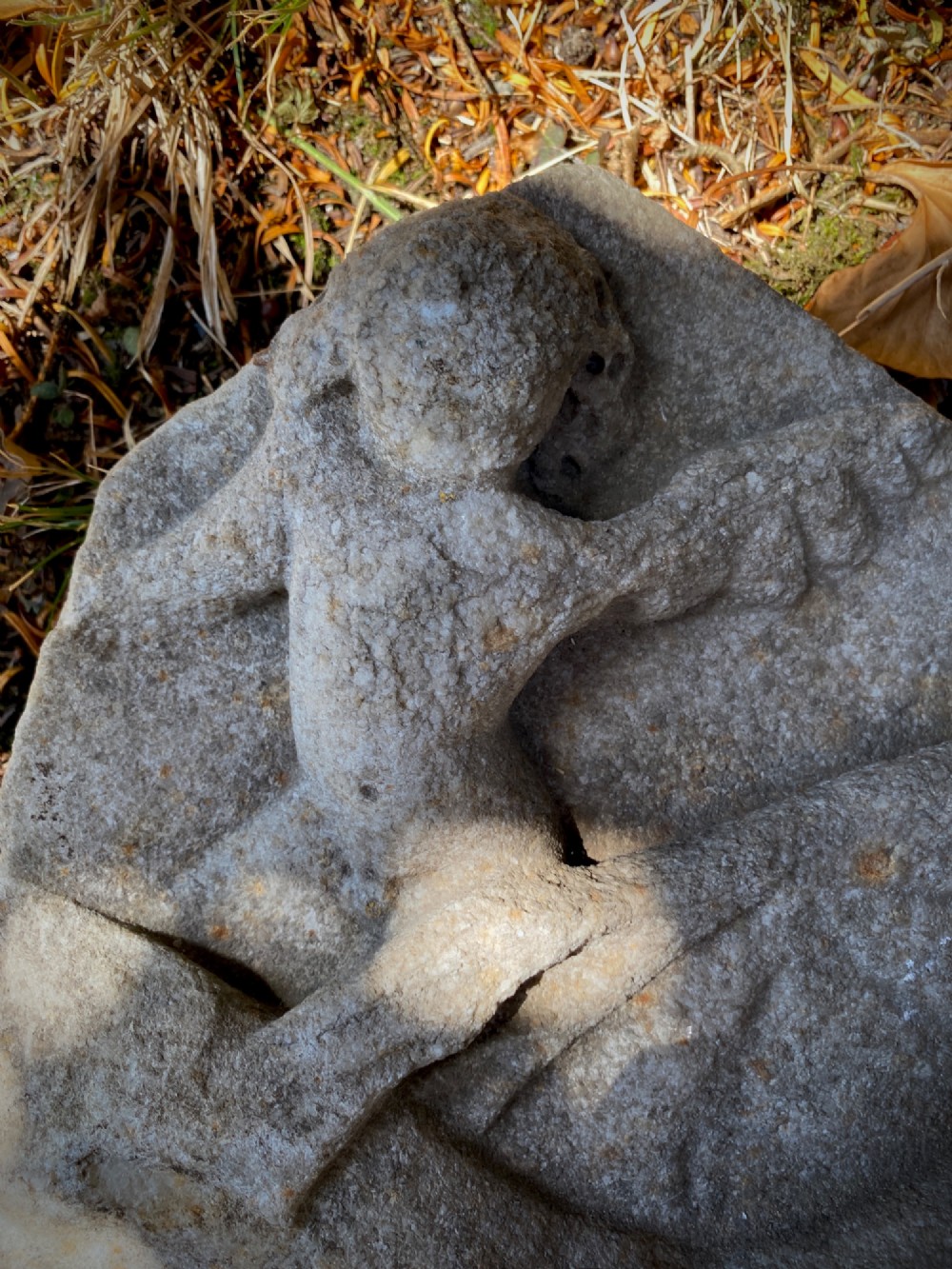 A carved weathered stone fragment depicting a high-relief figure of a winged cherub above a reclining form. View XI