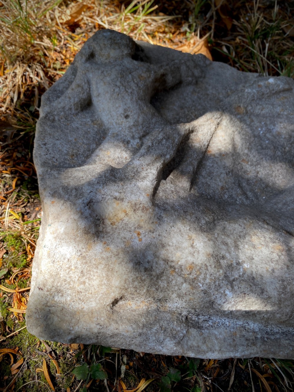A carved weathered stone fragment depicting a high-relief figure of a winged cherub above a reclining form. View XII