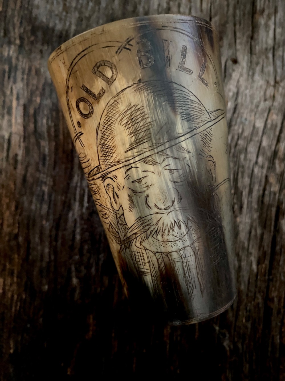 A translucent natural horn beaker featuring a detailed line engraving of the Bruce Bairnsfather character Old Bill wearing a helmet.