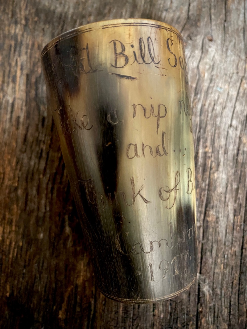 A translucent natural horn beaker featuring a detailed line engraving of the Bruce Bairnsfather character Old Bill wearing a helmet. View IV
