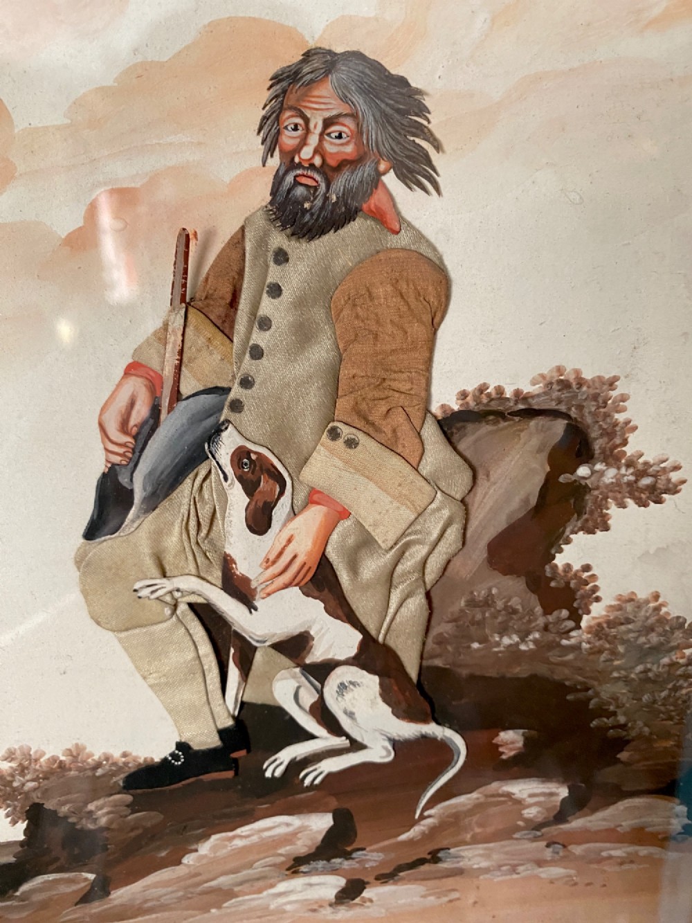 A late 18th-century Georgian folk art picture depicting a seated gamekeeper in fabric attire resting his hand on a spotted dog.