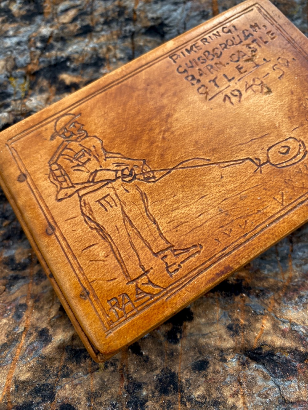 A rectangular carved wooden box lid depicting a uniformed military figure with a detector alongside hand-incised lettering detailing UK locations and dates. View II