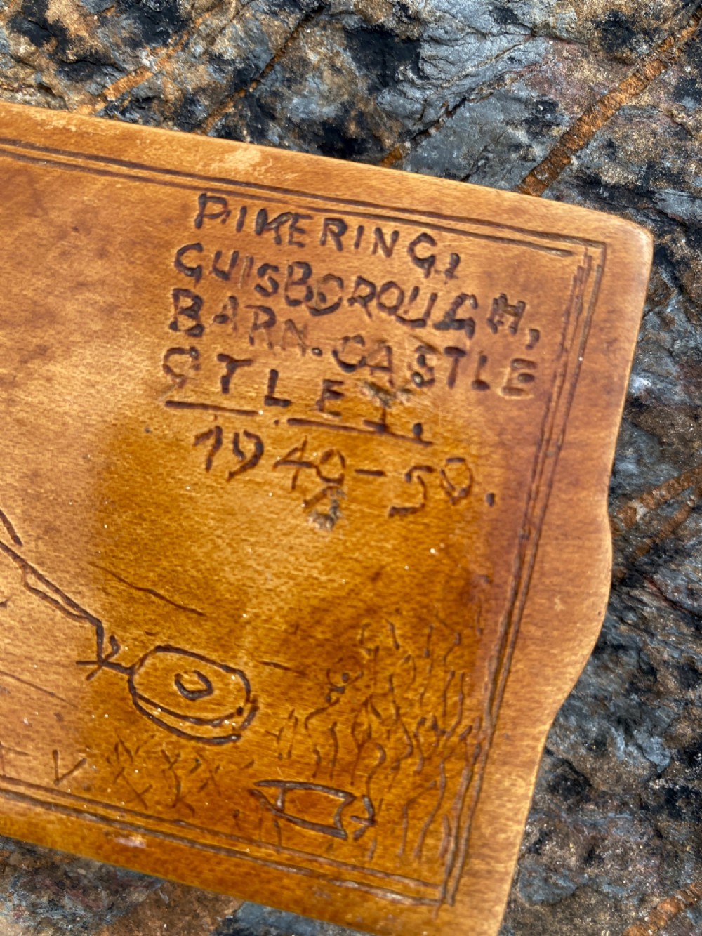 A rectangular carved wooden box lid depicting a uniformed military figure with a detector alongside hand-incised lettering detailing UK locations and dates. View III