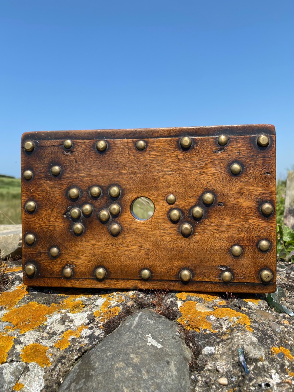 A rectangular low mahogany stool adorned with brass studs forming initials and a border around a central hand hole. View II
