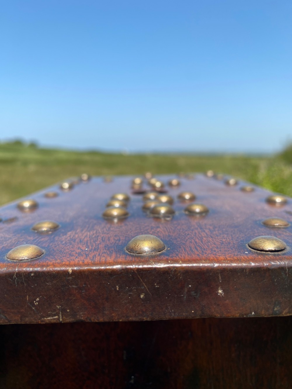 A rectangular low mahogany stool adorned with brass studs forming initials and a border around a central hand hole. View III