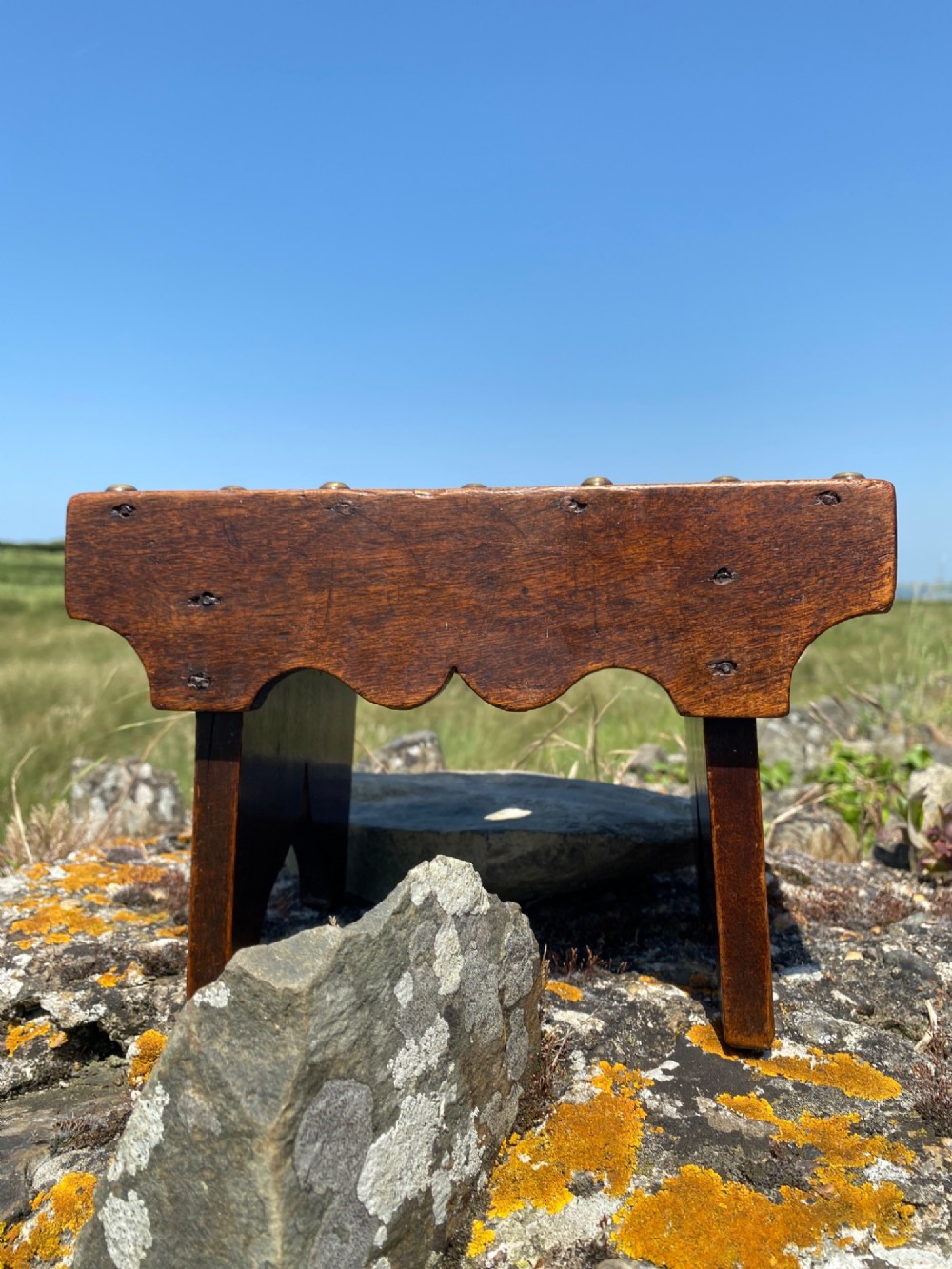 A rectangular low mahogany stool adorned with brass studs forming initials and a border around a central hand hole. View IV