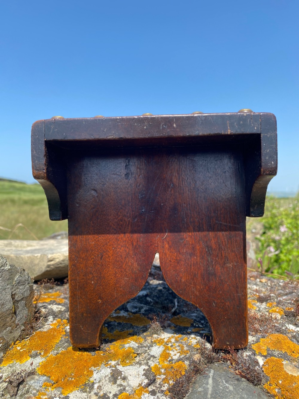 A rectangular low mahogany stool adorned with brass studs forming initials and a border around a central hand hole. View V