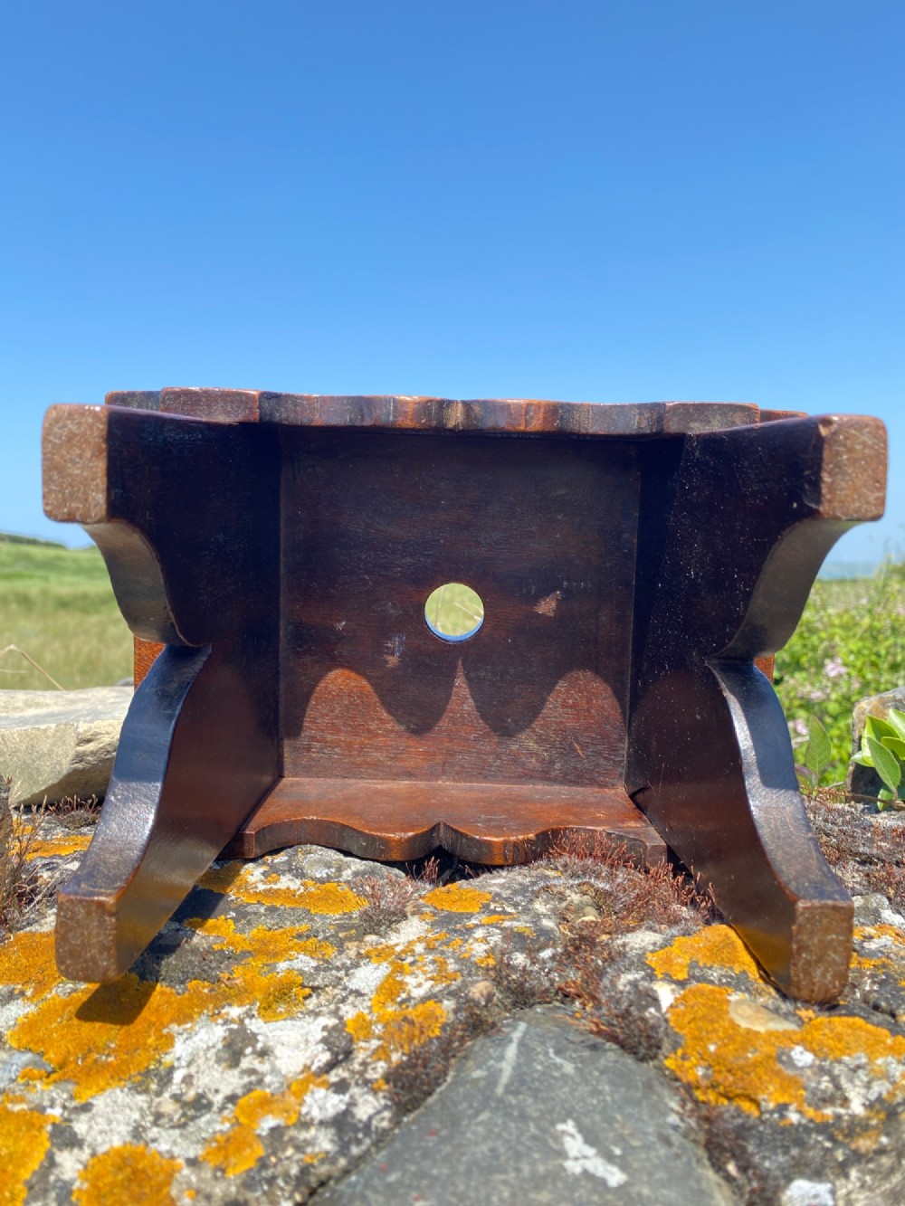 A rectangular low mahogany stool adorned with brass studs forming initials and a border around a central hand hole. View VI