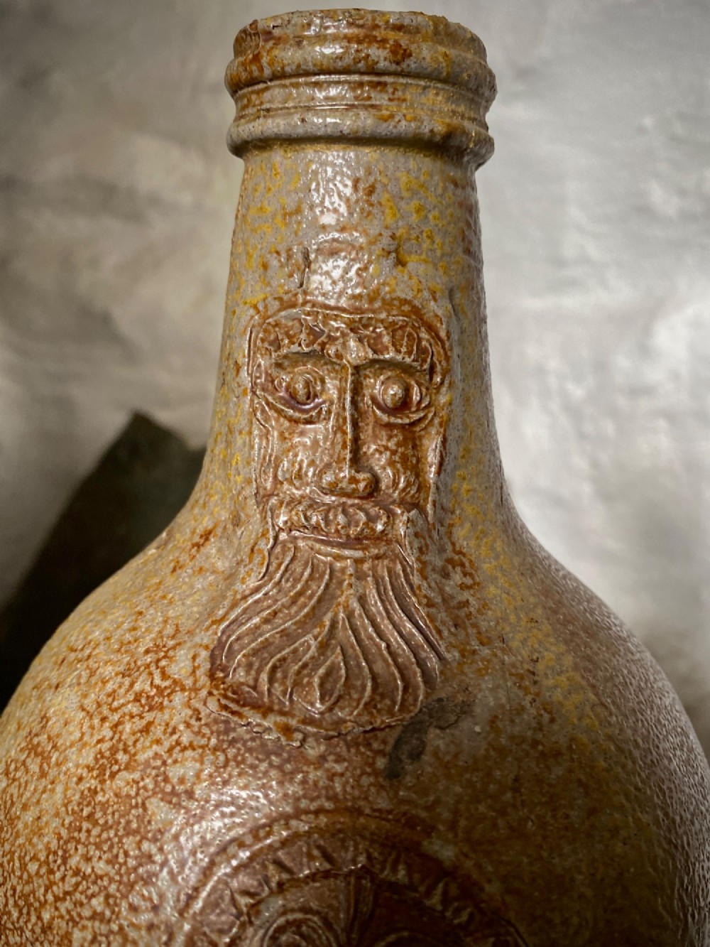 A salt-glazed stoneware Bartmann jug featuring a moulded bearded face mask on the neck and a round medallion crest on the globular body. View V