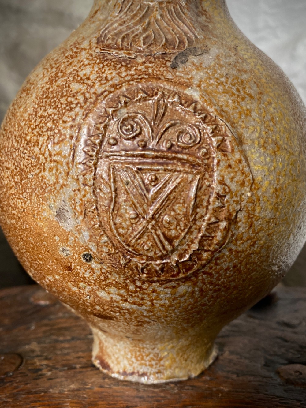 A salt-glazed stoneware Bartmann jug featuring a moulded bearded face mask on the neck and a round medallion crest on the globular body. View VII