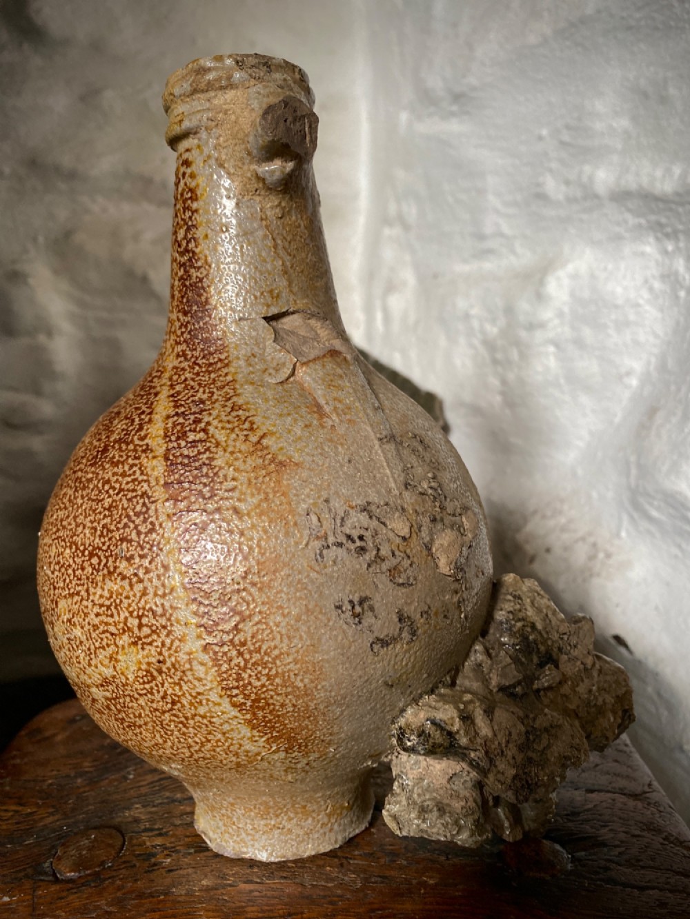 A salt-glazed stoneware Bartmann jug featuring a moulded bearded face mask on the neck and a round medallion crest on the globular body. View X