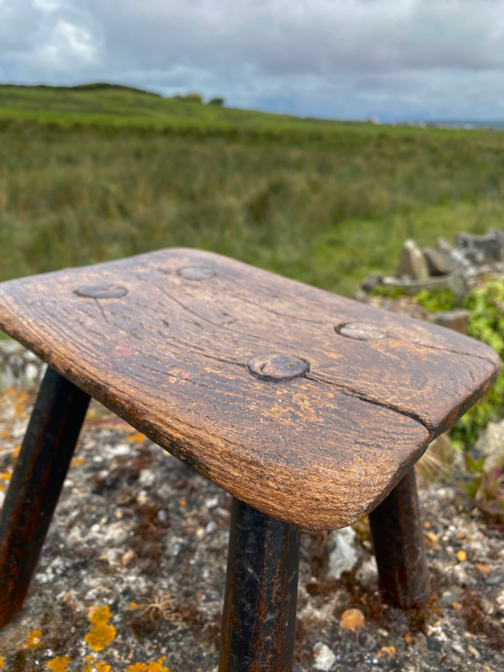 A low rectangular wooden hearth stool featuring dark aged oak timber, four splayed legs, and exposed wedged tenon joints on the top surface. View V