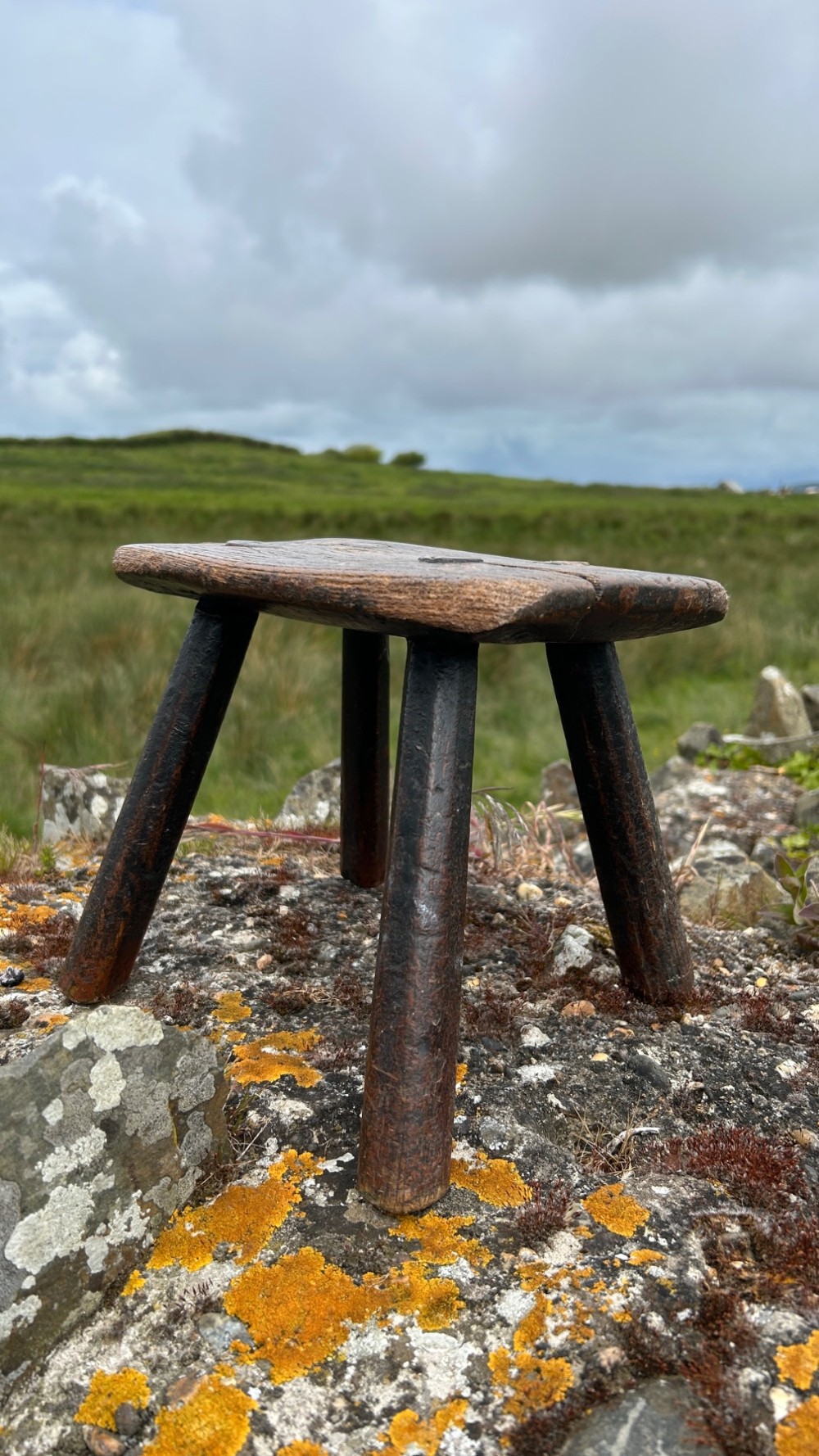 A low rectangular wooden hearth stool featuring dark aged oak timber, four splayed legs, and exposed wedged tenon joints on the top surface. View VII