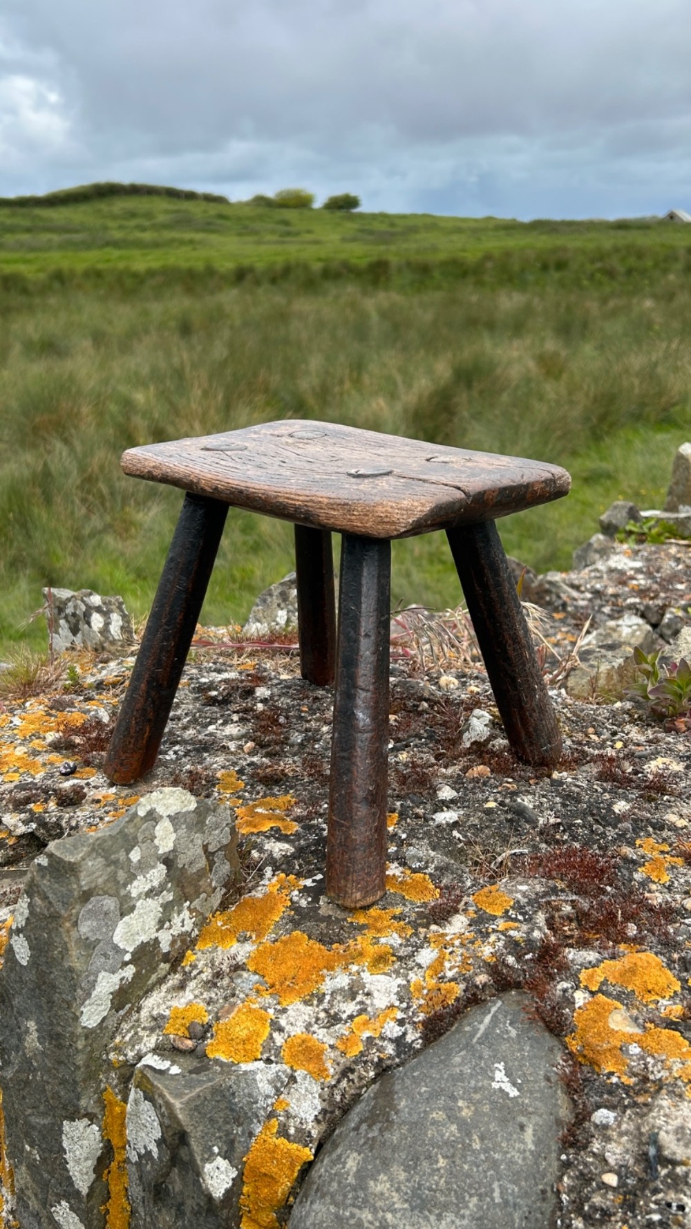 A low rectangular wooden hearth stool featuring dark aged oak timber, four splayed legs, and exposed wedged tenon joints on the top surface.