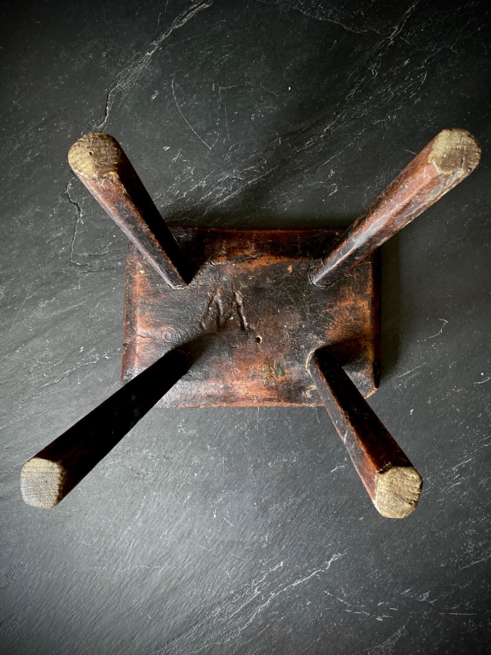 A low rectangular wooden hearth stool featuring dark aged oak timber, four splayed legs, and exposed wedged tenon joints on the top surface. View IX