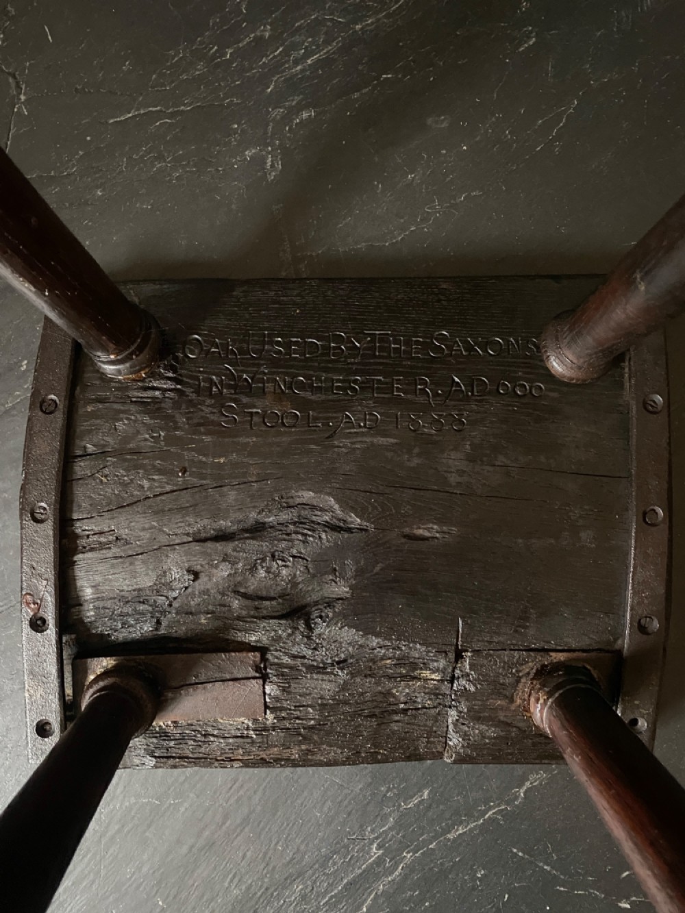 A dark brown carved oak stool featuring hand-carved shell motif decoration on the top seat and four turned wooden legs. View II