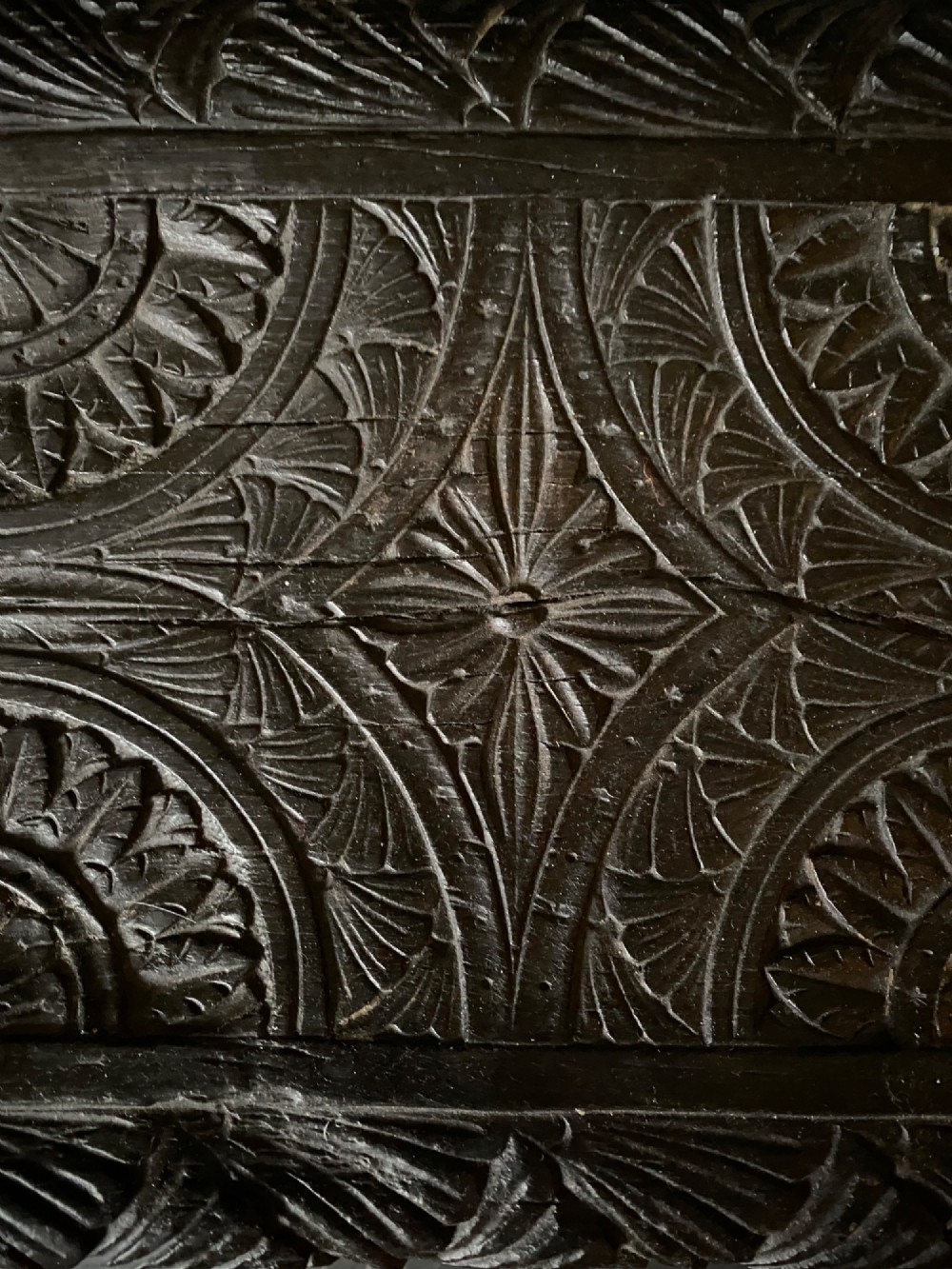 A dark brown carved oak stool featuring hand-carved shell motif decoration on the top seat and four turned wooden legs. View V