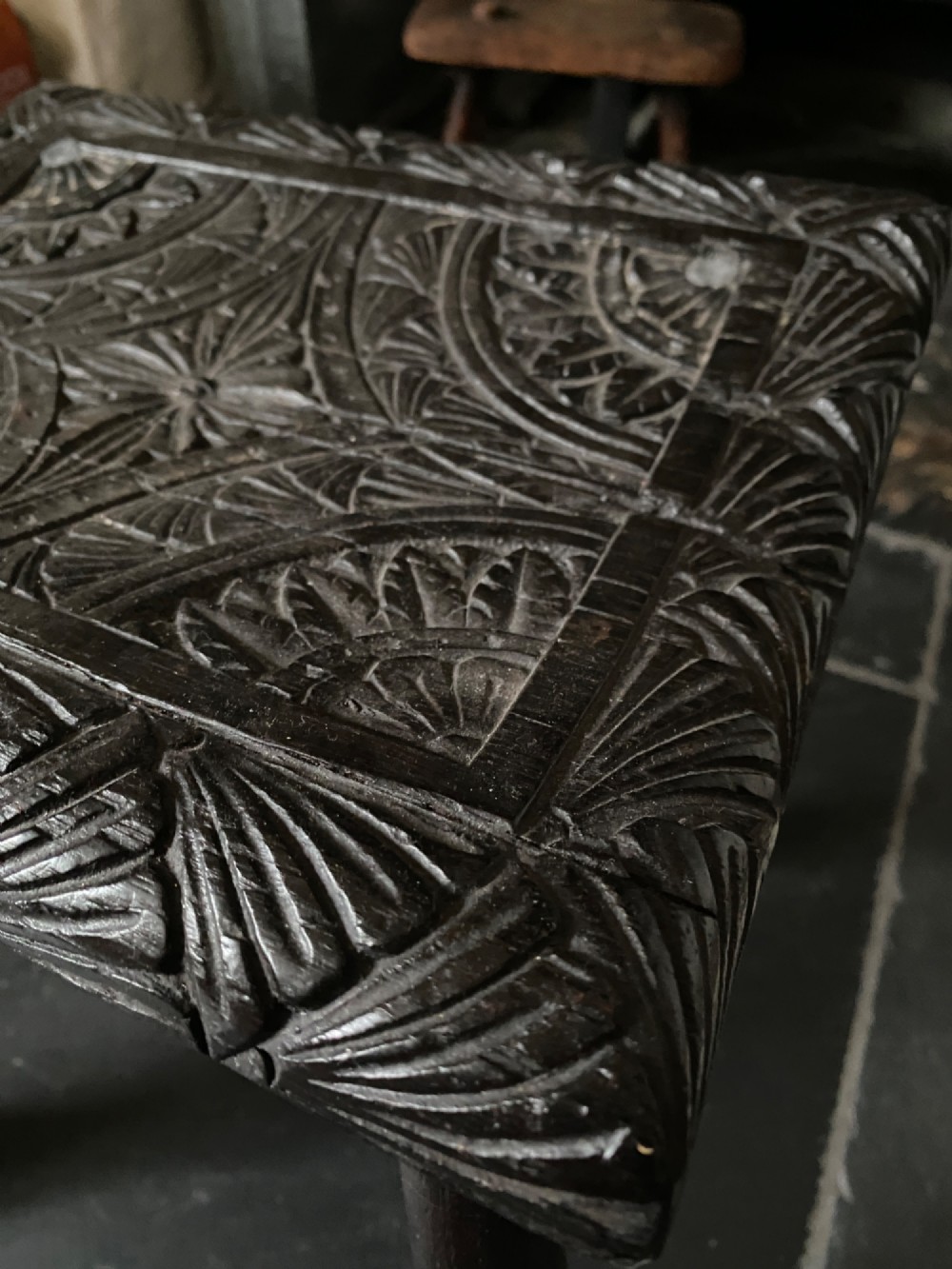 A dark brown carved oak stool featuring hand-carved shell motif decoration on the top seat and four turned wooden legs. View VI