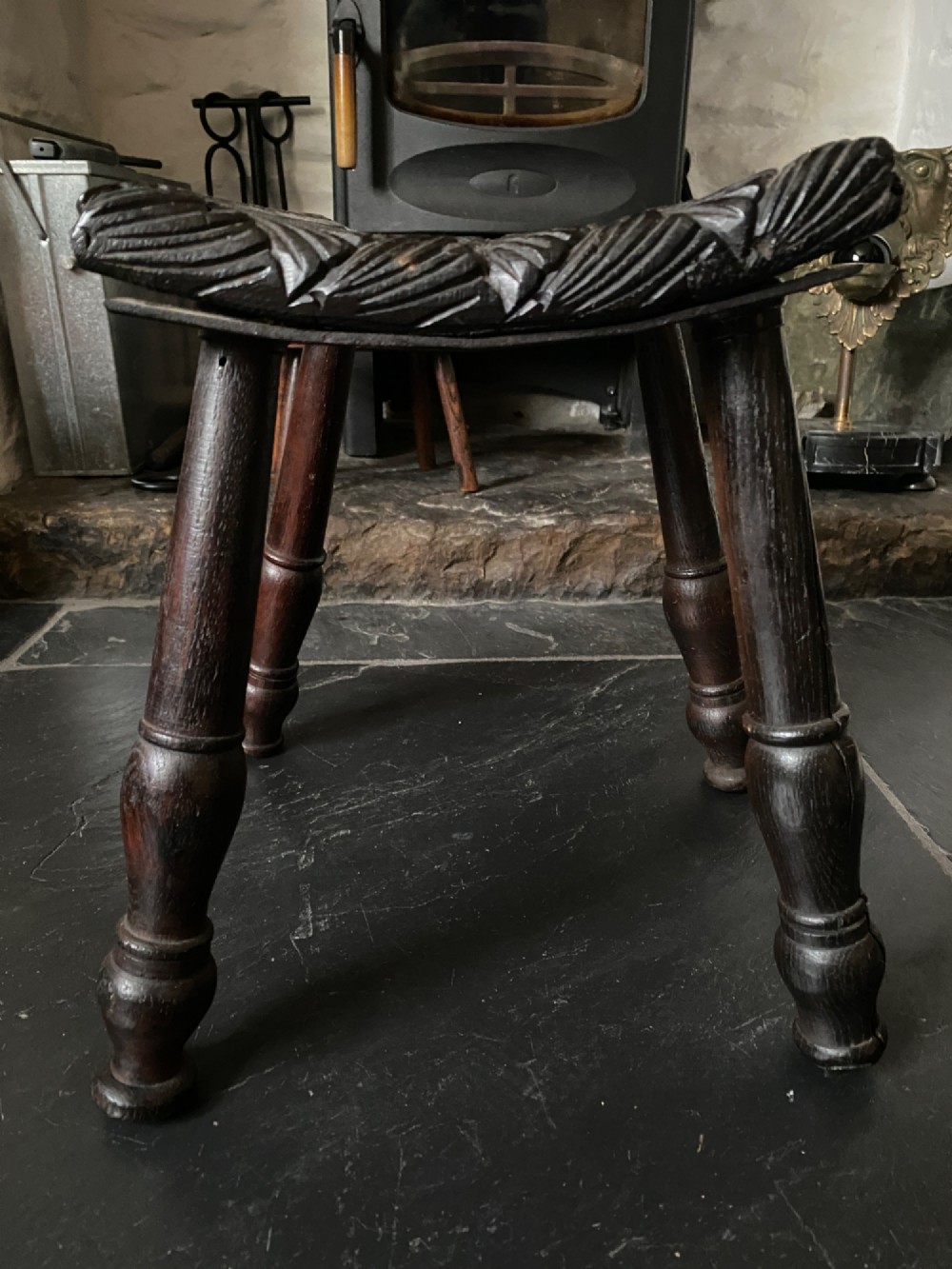 A dark brown carved oak stool featuring hand-carved shell motif decoration on the top seat and four turned wooden legs. View VII