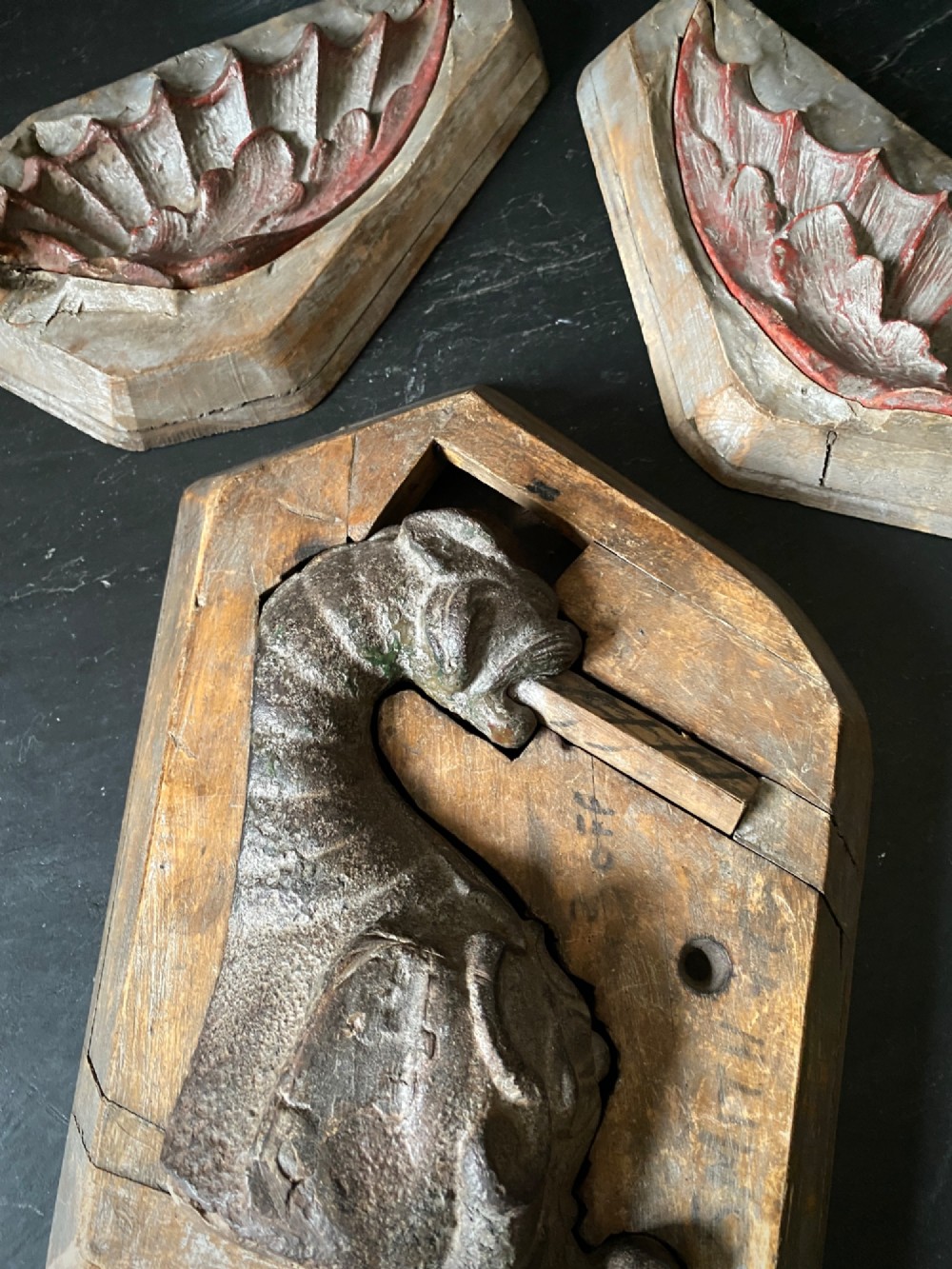 A three-piece set of carved wooden pattern moulds featuring a central seated gargoyle figure flanked by two bat-like wing panels with red paint accents. View VI
