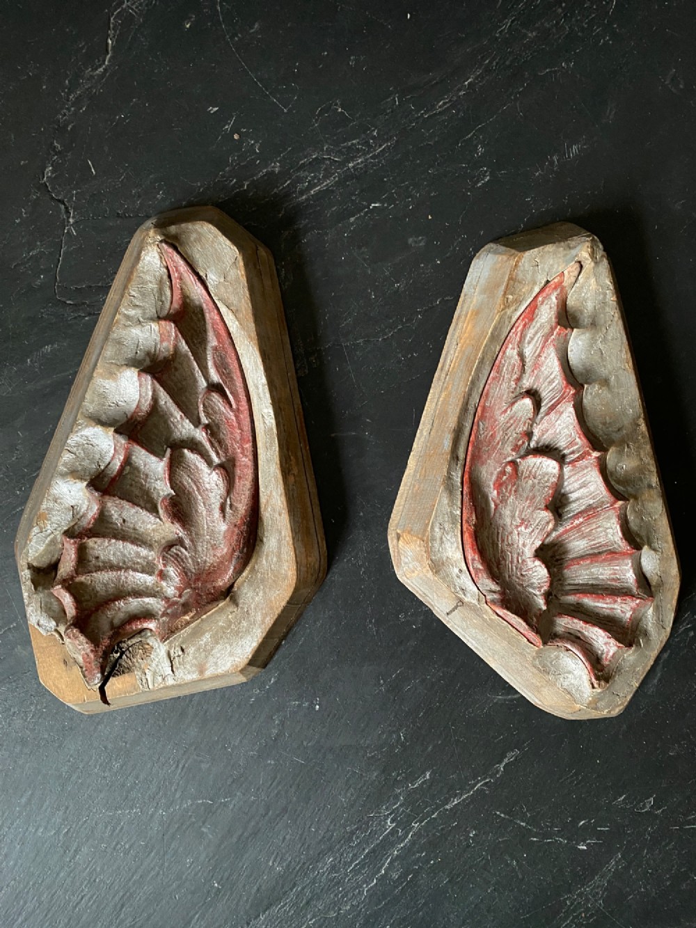 A three-piece set of carved wooden pattern moulds featuring a central seated gargoyle figure flanked by two bat-like wing panels with red paint accents. View VII