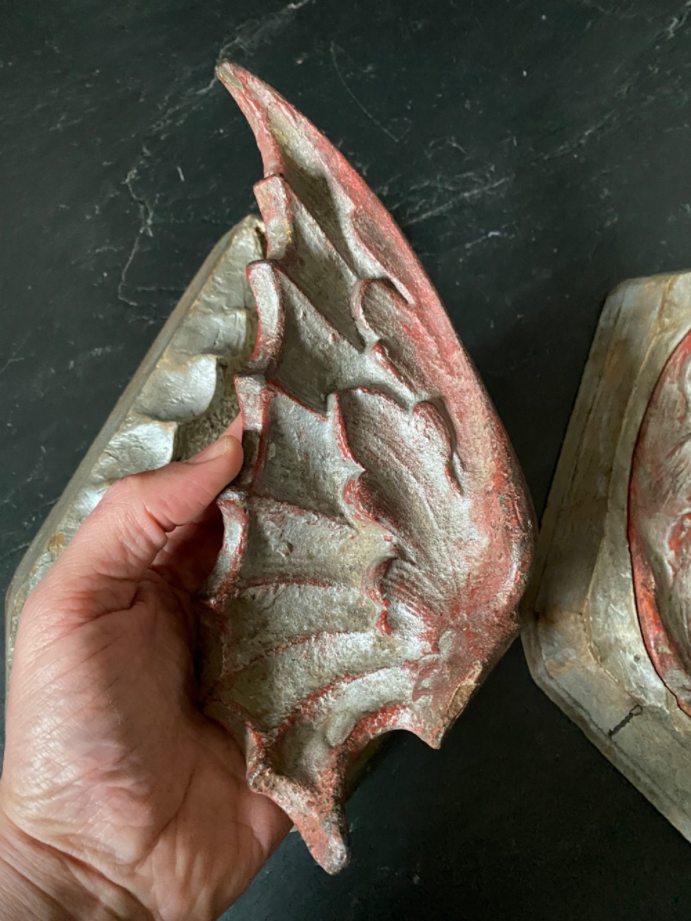 A three-piece set of carved wooden pattern moulds featuring a central seated gargoyle figure flanked by two bat-like wing panels with red paint accents. View IX