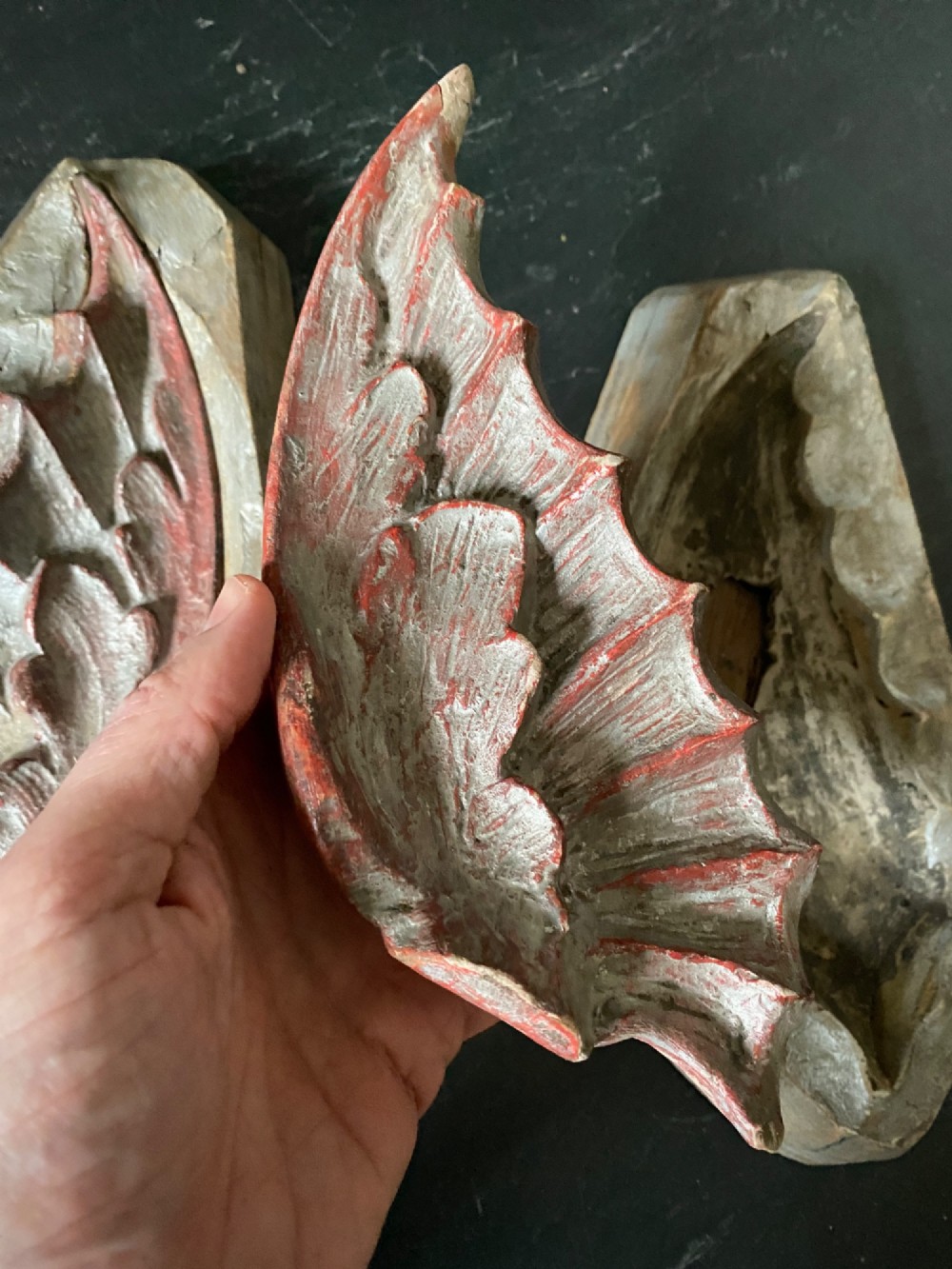 A three-piece set of carved wooden pattern moulds featuring a central seated gargoyle figure flanked by two bat-like wing panels with red paint accents. View XI