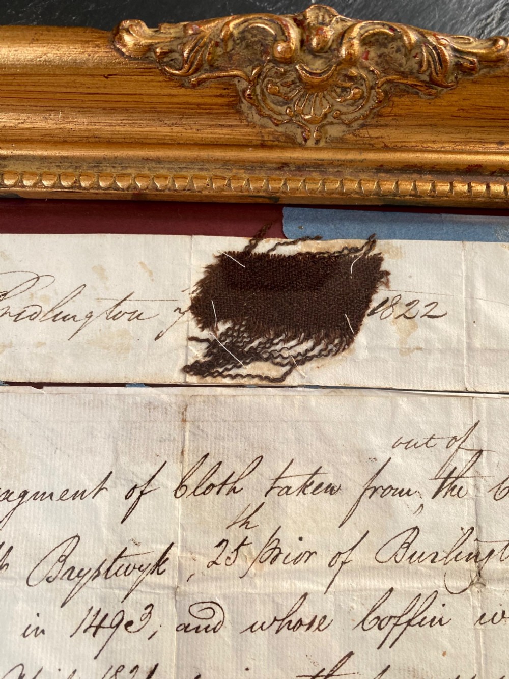 A dark 15th-century textile fragment and handwritten 19th-century note mounted inside an ornate carved giltwood frame. View III