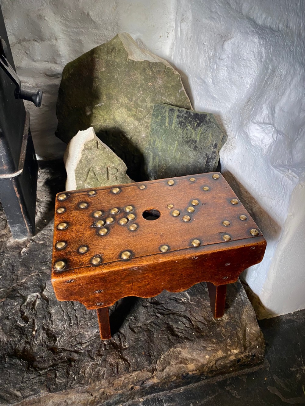 A rectangular low mahogany stool adorned with brass studs forming initials and a border around a central hand hole.