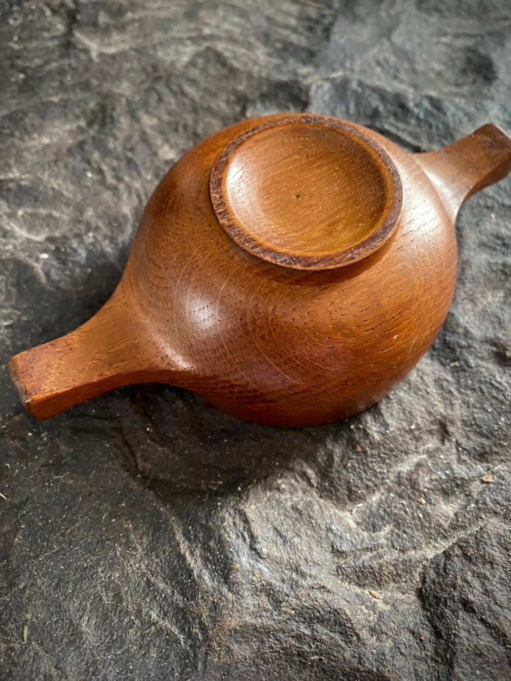 A small carved wooden quaich featuring two side handles and an aged handwritten paper label attached to the front bowl. View V