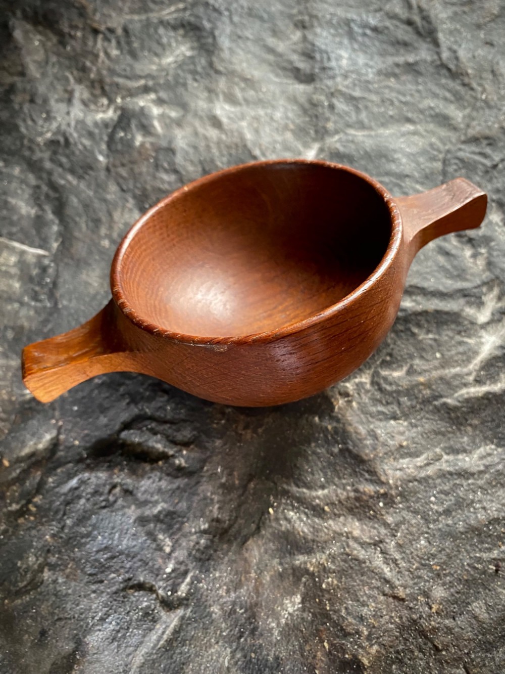 A small carved wooden quaich featuring two side handles and an aged handwritten paper label attached to the front bowl. View VI