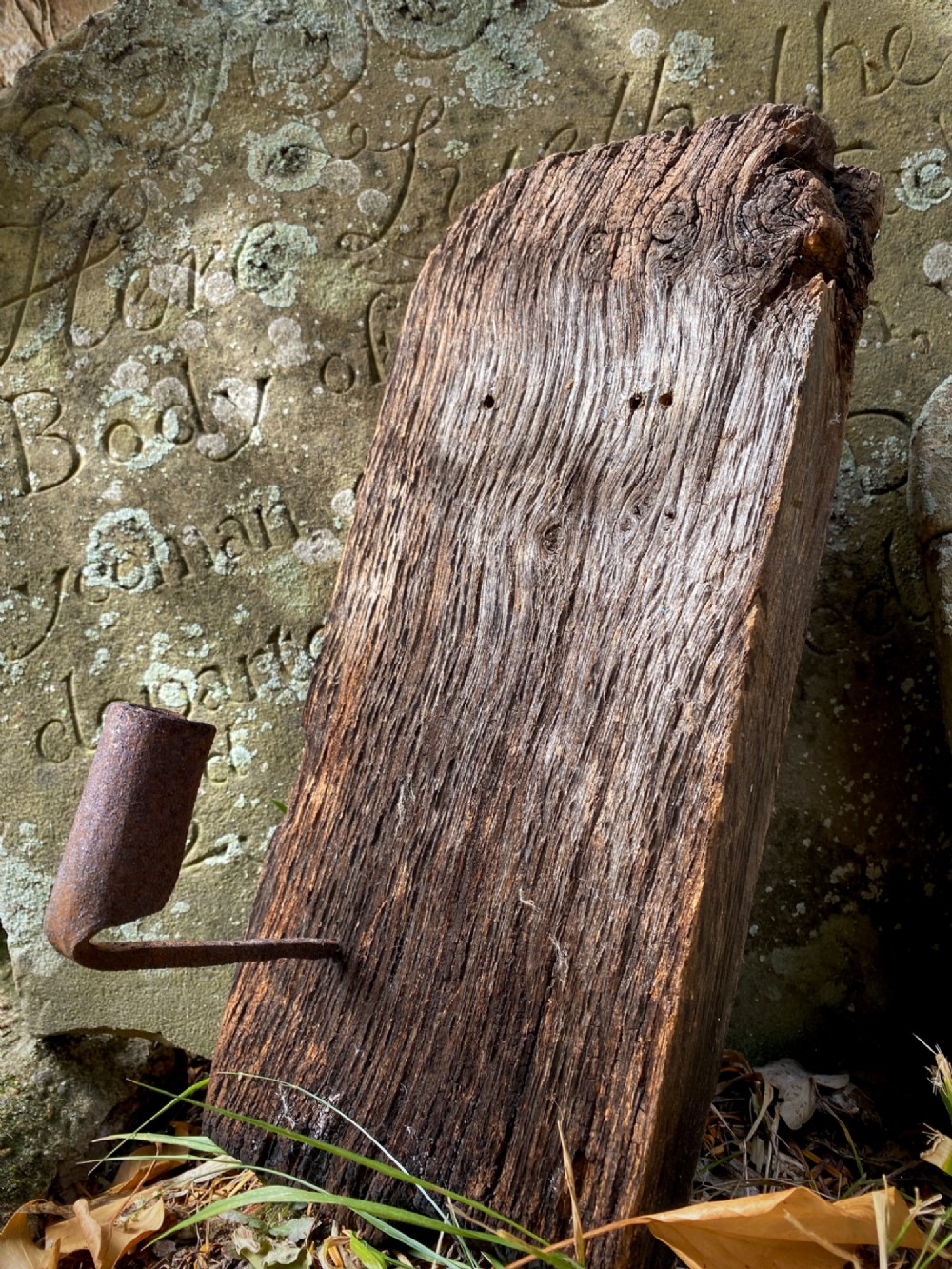 A primitive hand-forged wrought iron candle socket mounted on a pointed spike inserted into a thick piece of weathered timber.