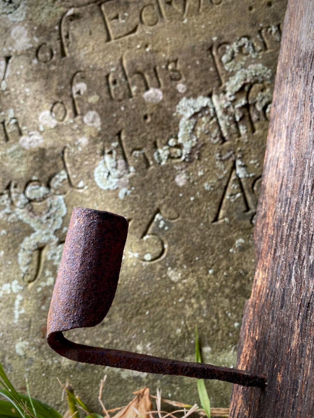 A primitive hand-forged wrought iron candle socket mounted on a pointed spike inserted into a thick piece of weathered timber. View II