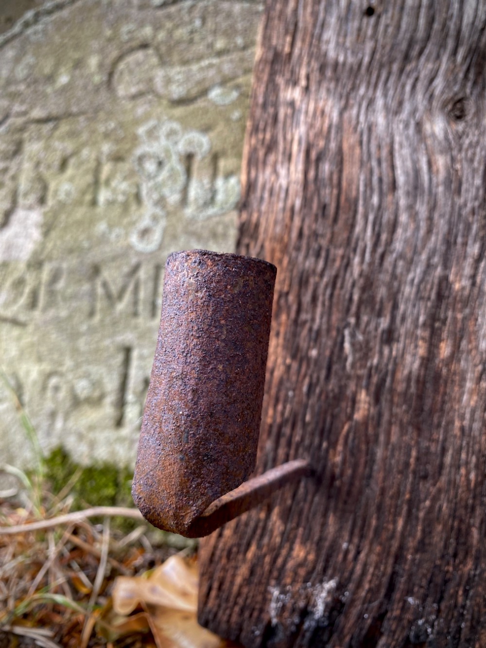 A primitive hand-forged wrought iron candle socket mounted on a pointed spike inserted into a thick piece of weathered timber. View III