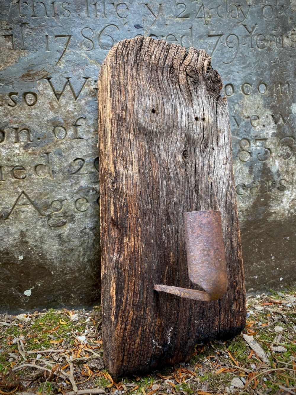 A primitive hand-forged wrought iron candle socket mounted on a pointed spike inserted into a thick piece of weathered timber. View IV